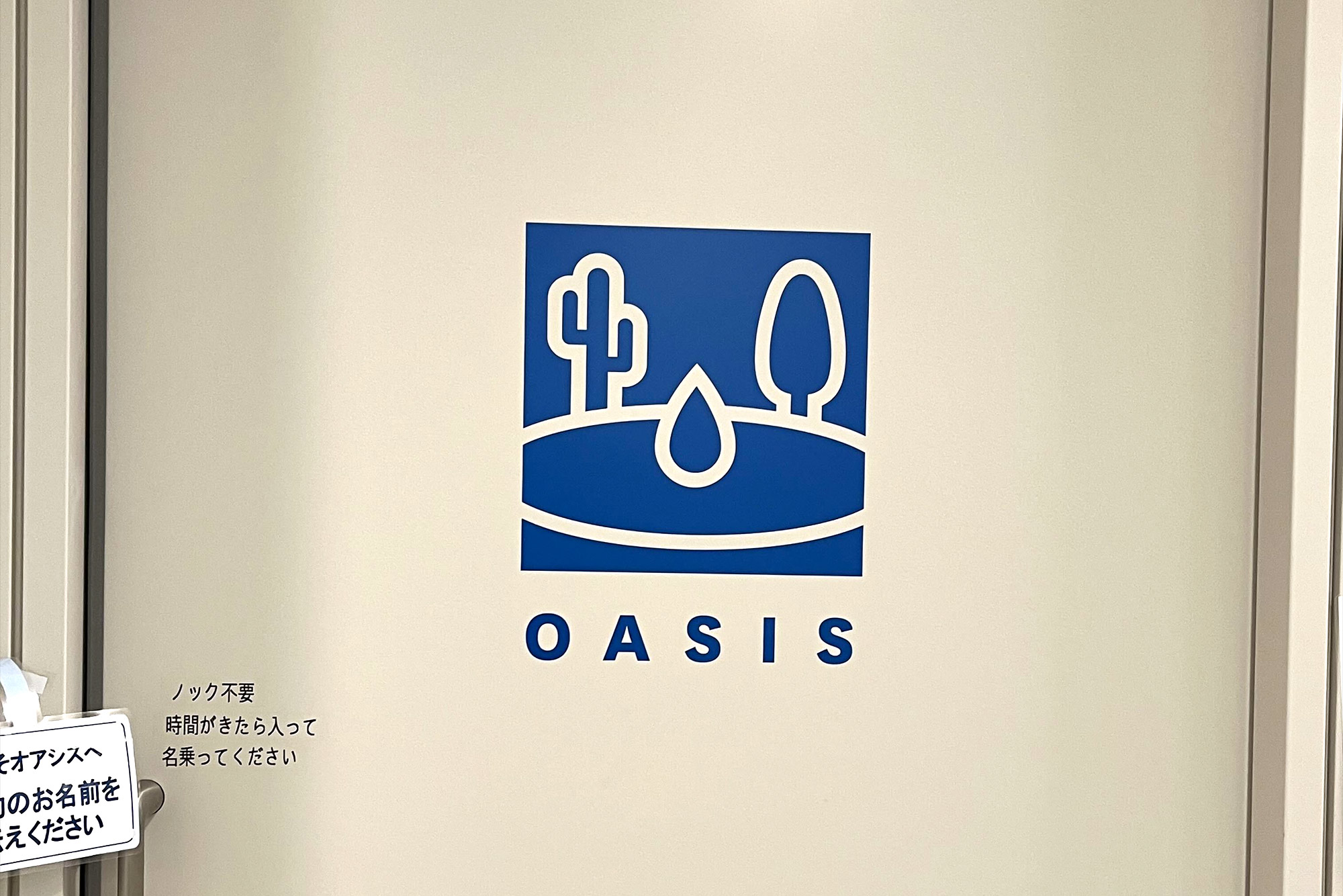 フリー株式会社のオフィスにあるマッサージルーム「OASIS」の入口 大きなロゴが描かれた引き戸の取手の上部に「ノック不要 時間がきたら入って名乗ってください」と印字されている